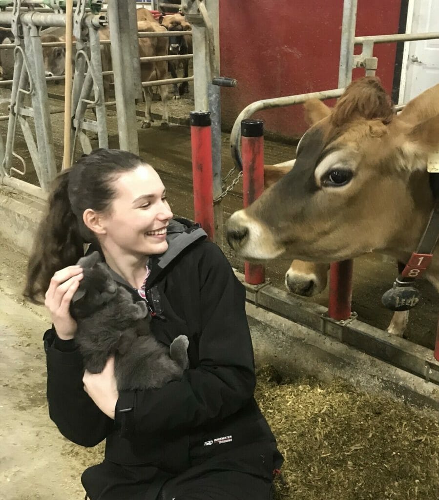 Victoria Ryan holding a cat and smiling at a cow